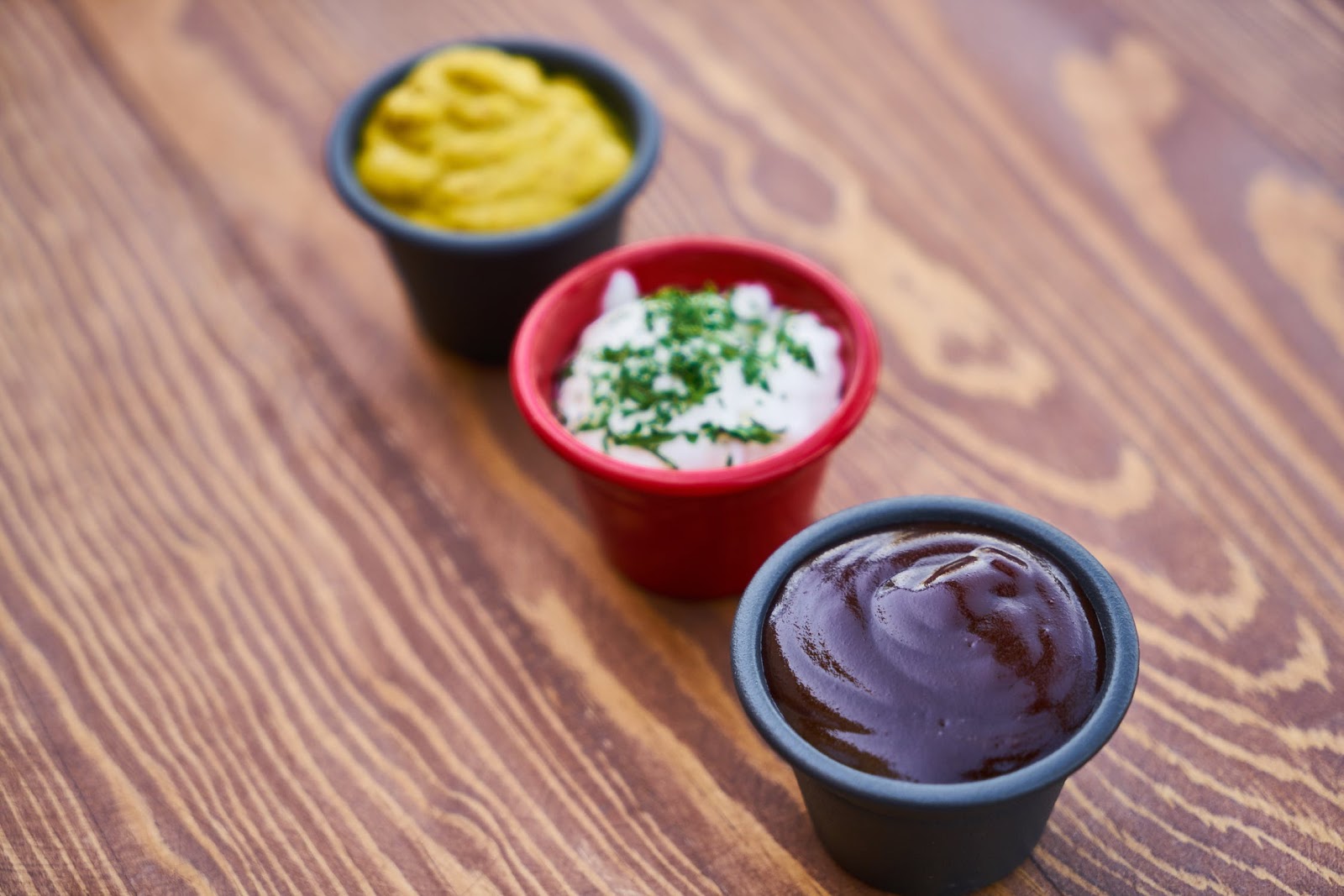 Trio of small condiment containers including mustard, mayo, and BBQ sauce