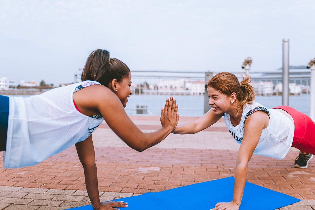 Two women doing push-ups while doing a hand touch